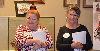 Two OLLI member smiling to the camera while holding registration papers